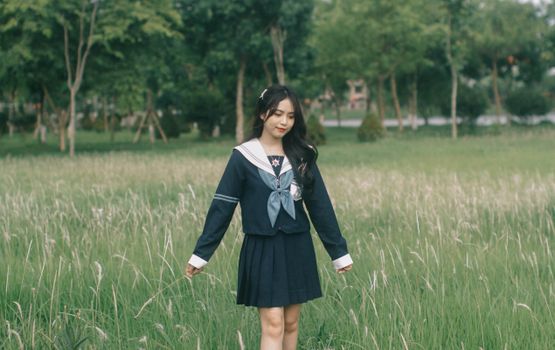 A young woman in a school uniform enjoying a walk through a green field on a sunny day.