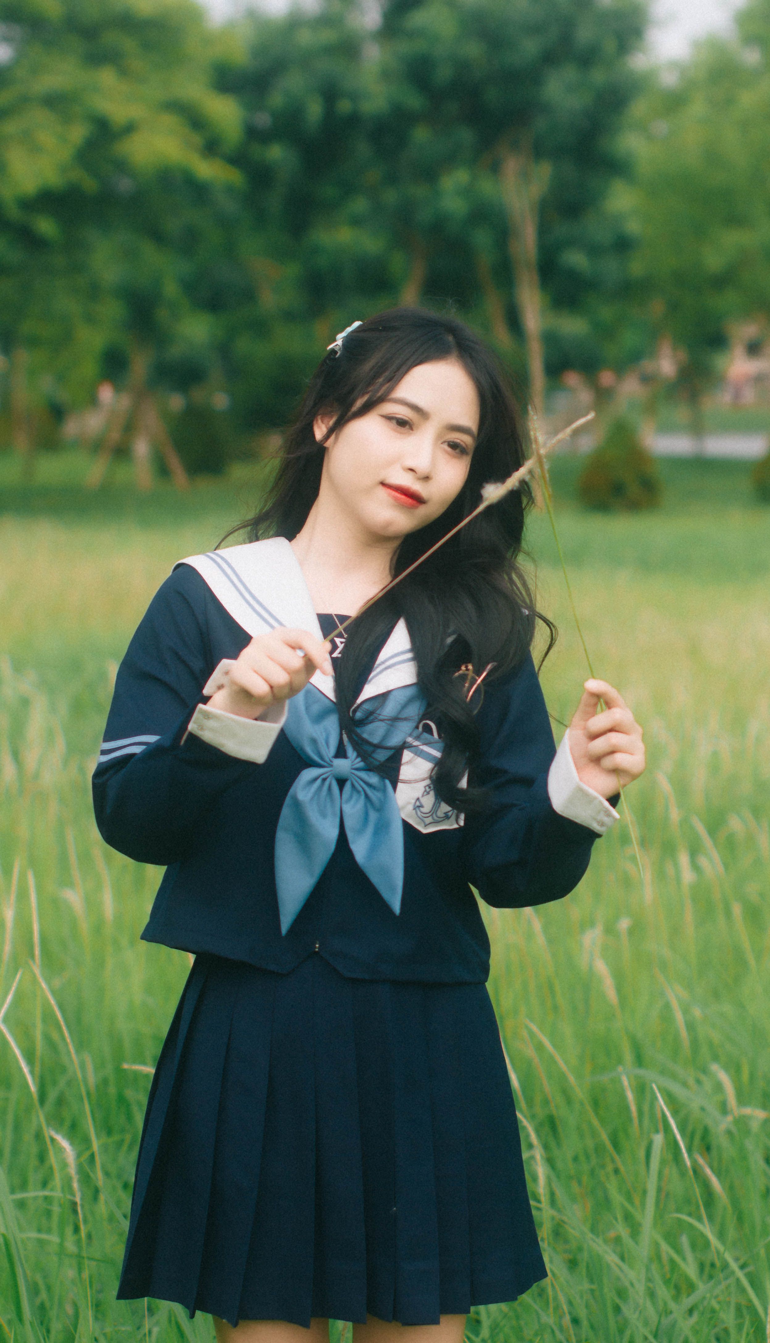 A young woman in a sailor uniform enjoys a peaceful moment outdoors in a lush green park.
