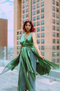 A stylish woman in a green dress poses confidently on an urban balcony with a cityscape backdrop.