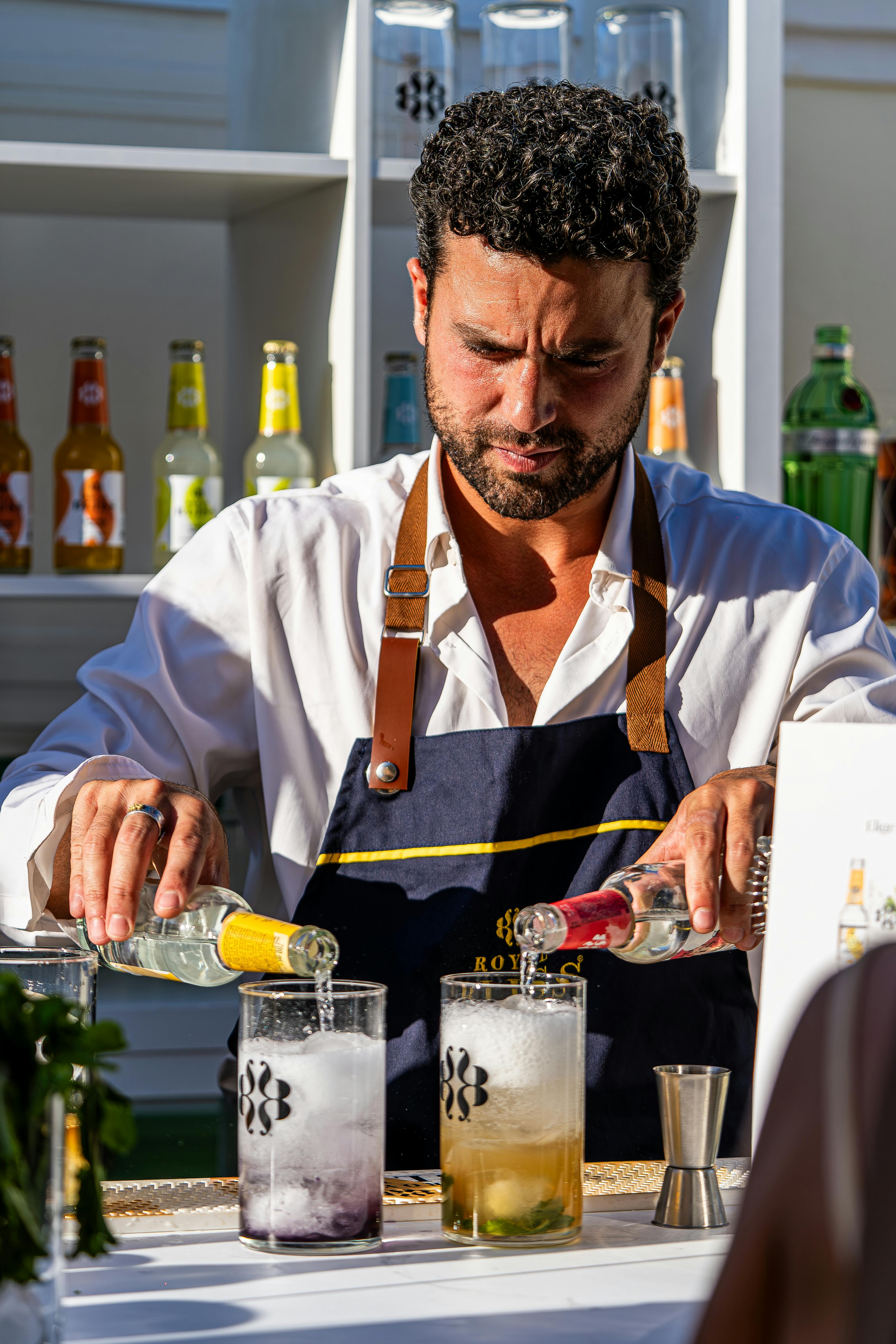 Bartender expertly crafting cocktails with bottles and garnishes at an outdoor bar, showcasing mixology skills.
