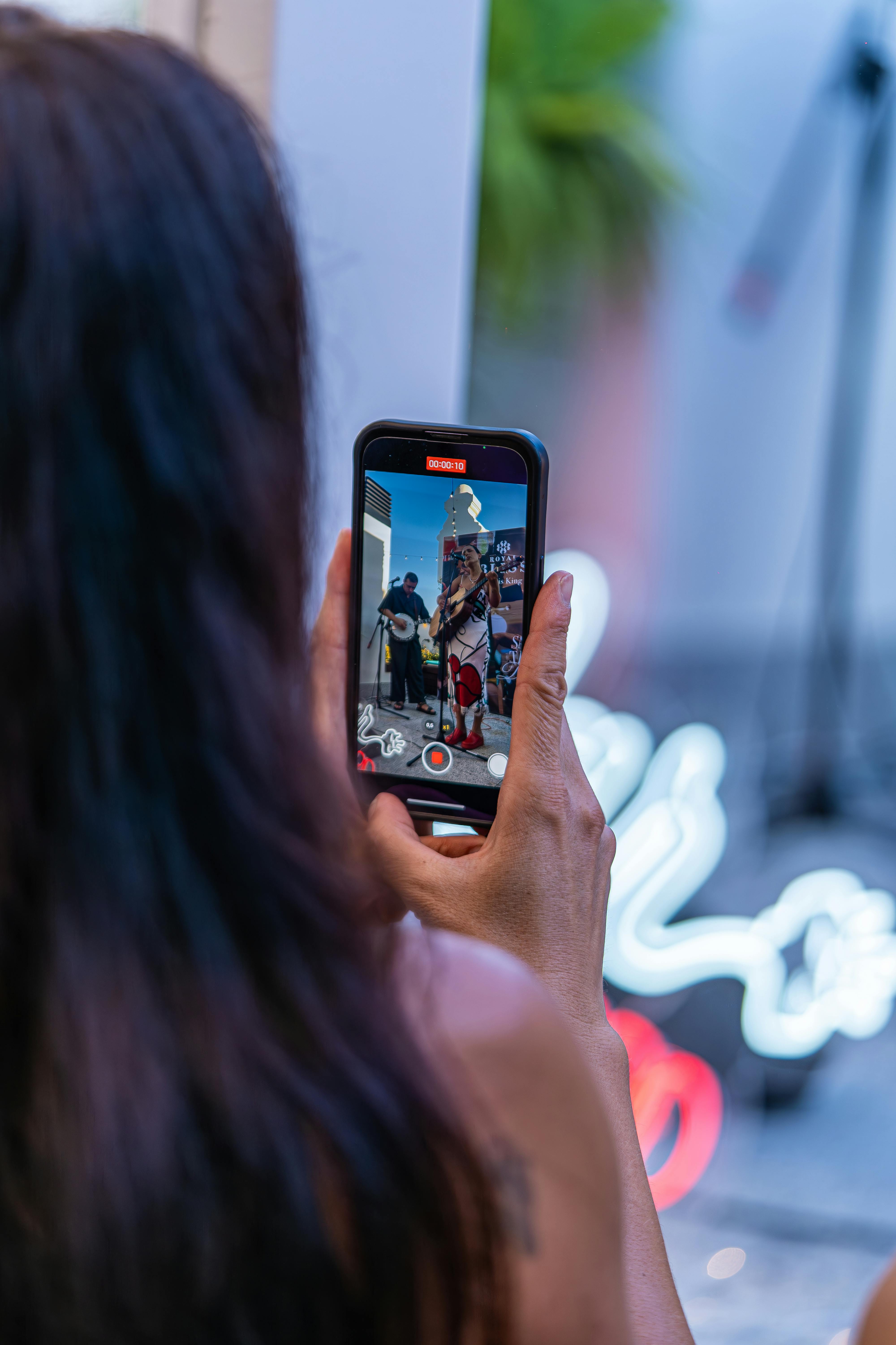 Woman records a live band on her smartphone amidst neon lights.