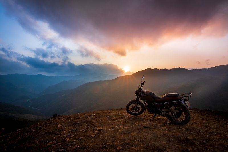 A motorcycle on a mountain trail silhouetted against a breathtaking sunset view