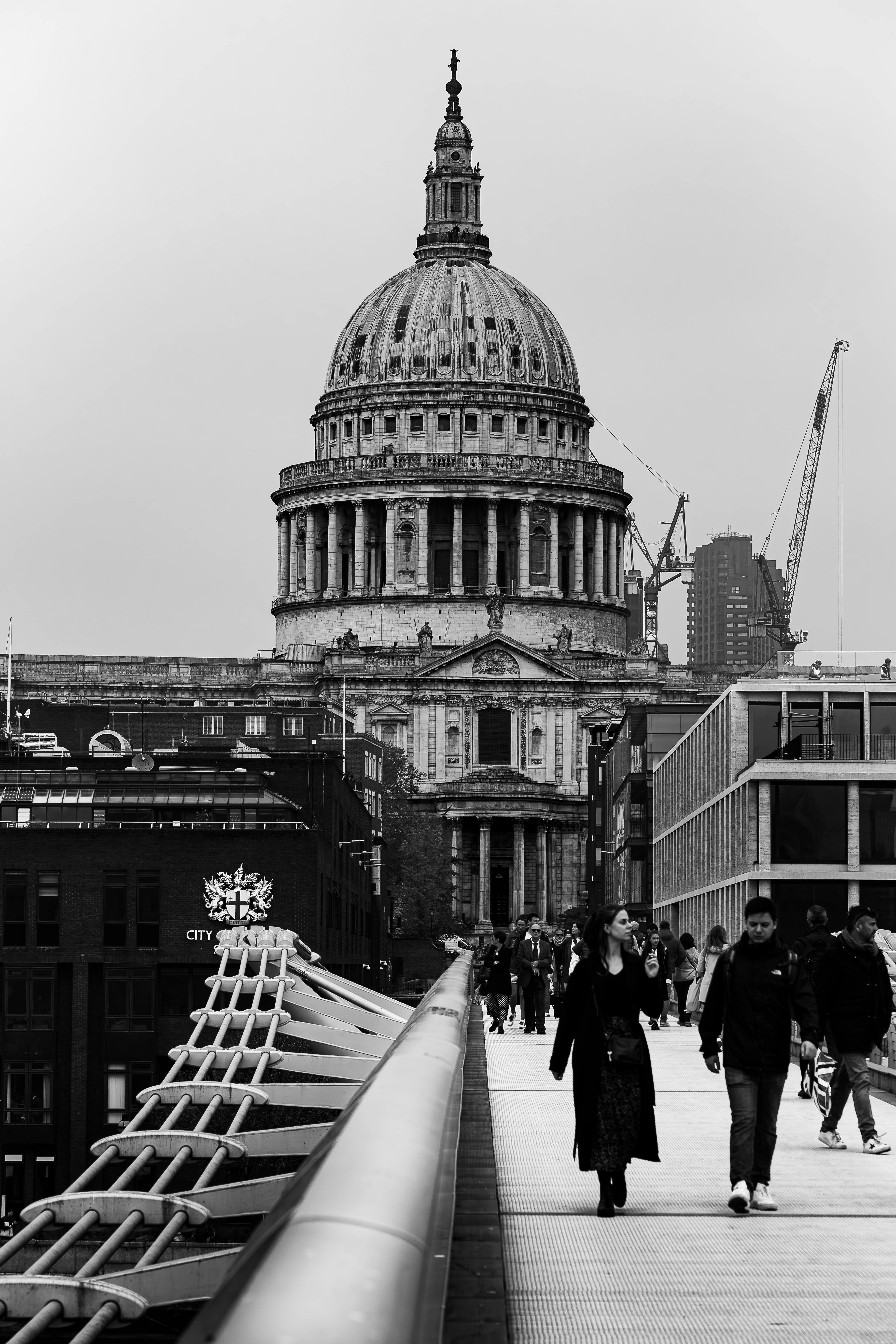 A monochrome view of people crossing the Millennium Bridge towards a historic cathedral, capturing urban architecture.