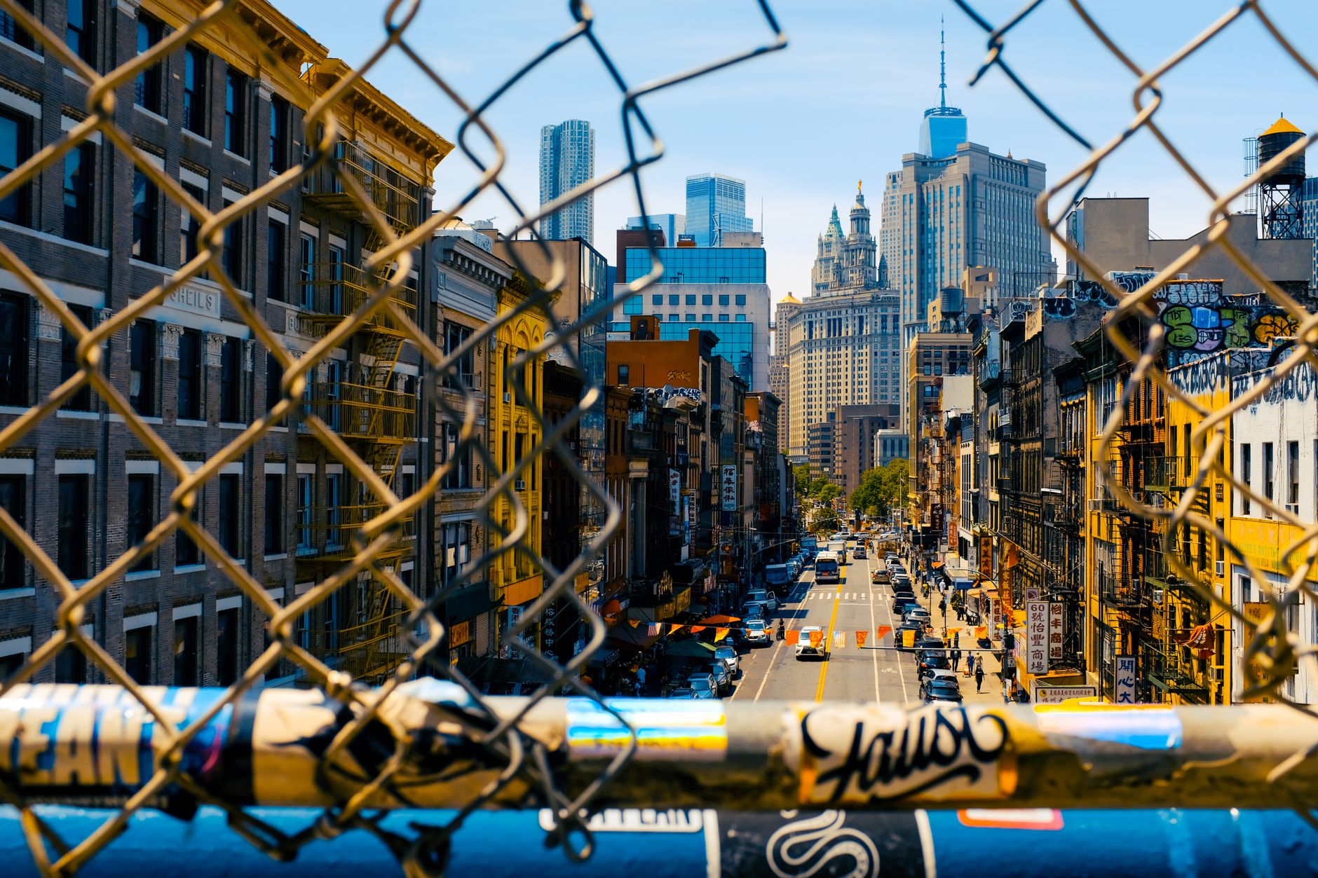 Explore a vibrant urban scene through a chain-link fence, capturing New York City's lively streets.
