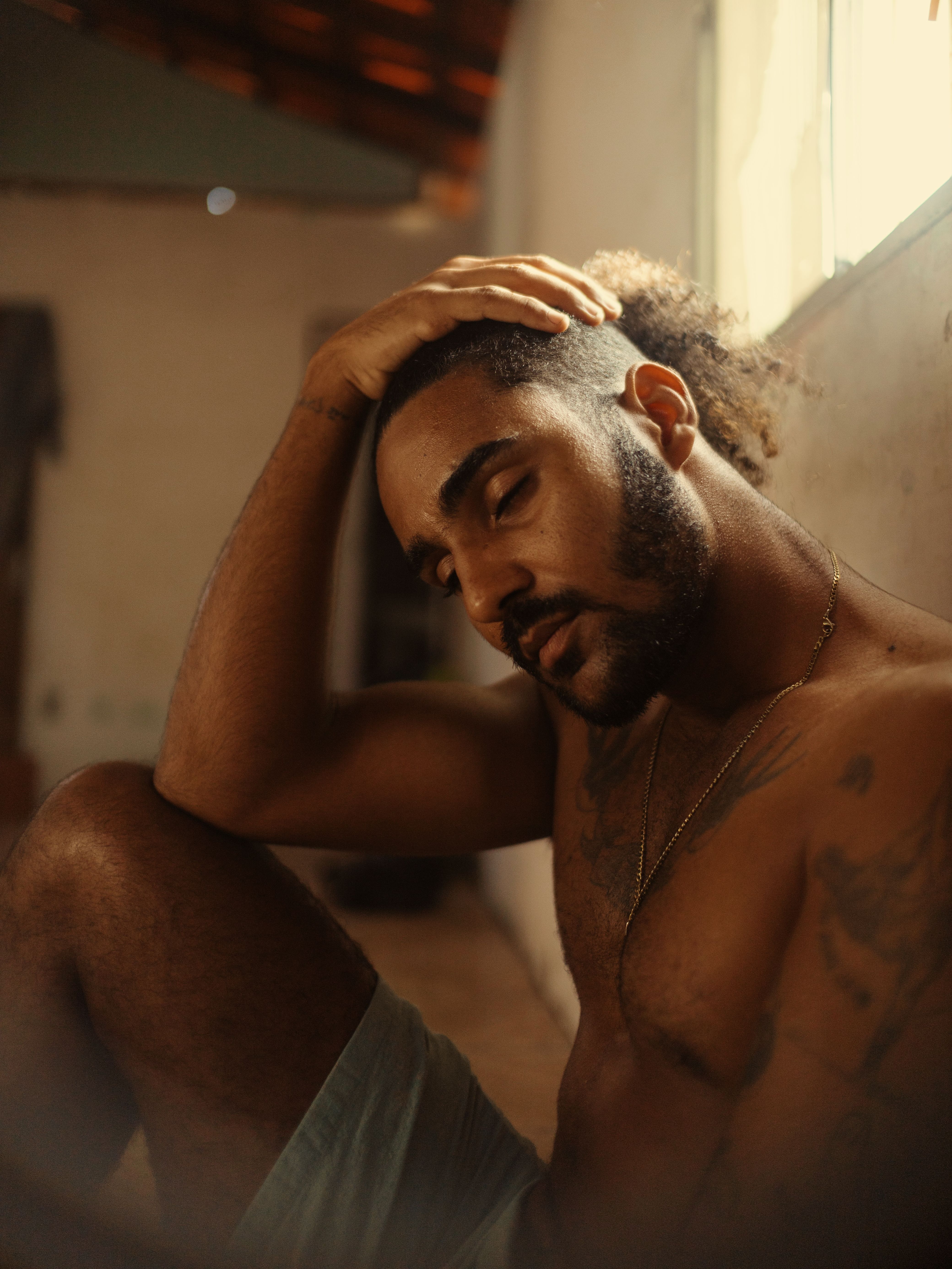 Artistic portrait of a tattooed man with eyes closed, in a warm indoor setting.