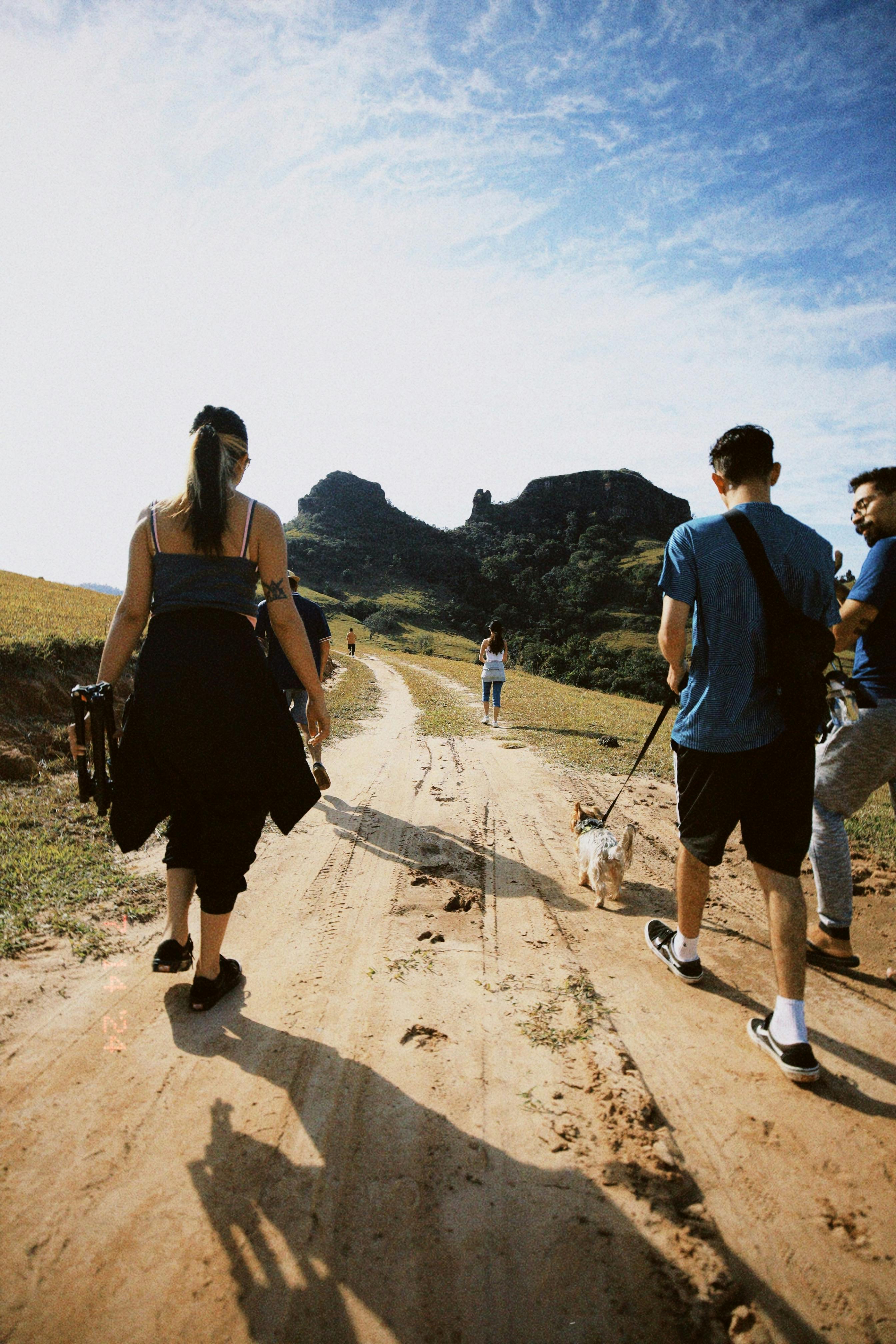 a group of people walking down a dirt road with a dog