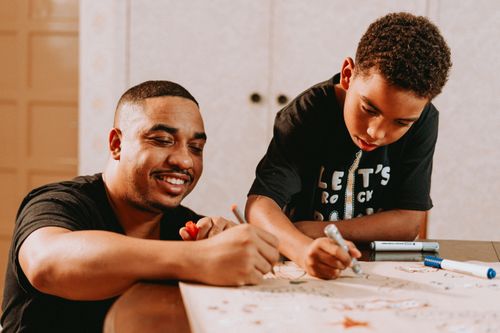 Free Father and son happily drawing together at home, fostering creativity and family bonding. Stock Photo