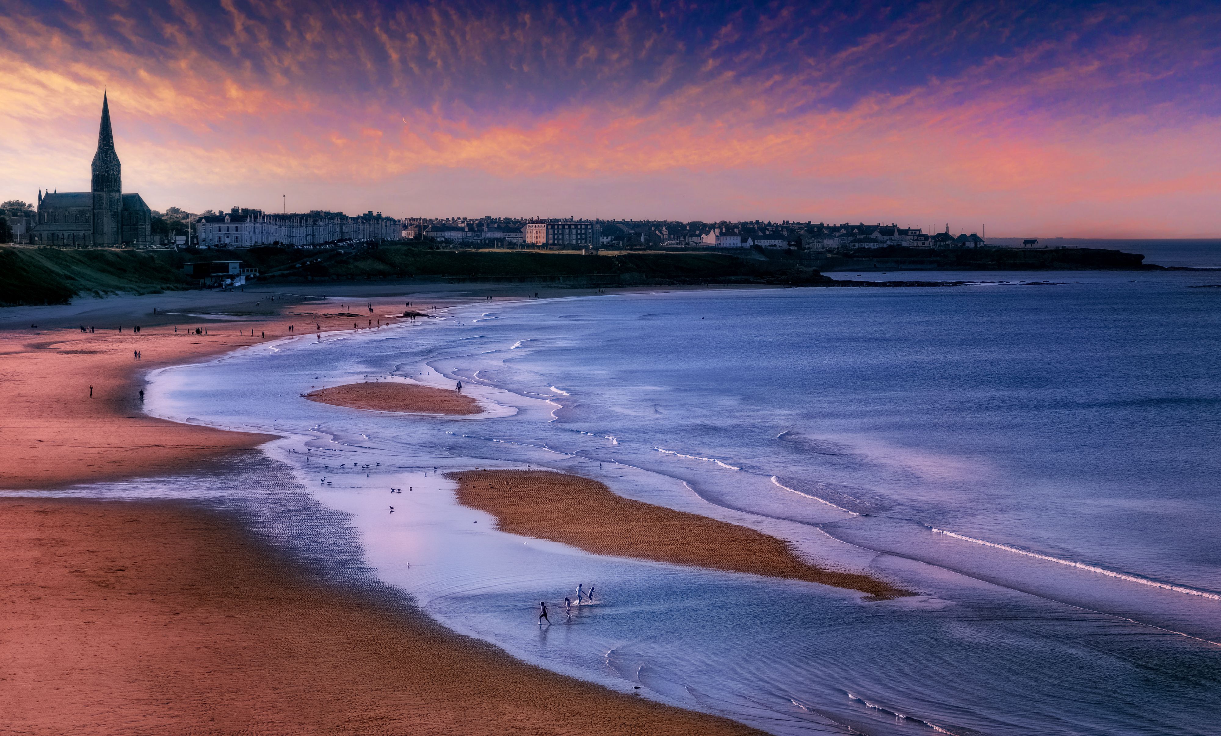 A beach with a sunset and a city skyline · Free Stock Photo