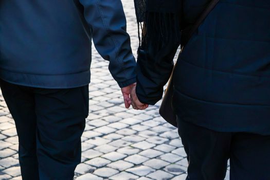 Back view of a couple holding hands walking on a cobblestone street.