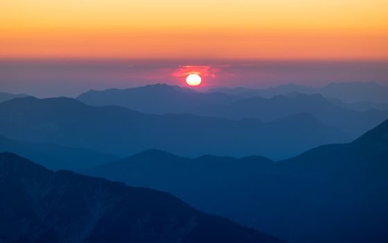 A breathtaking sunset over layered mountain ranges, capturing serene natural beauty.
