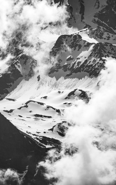 Black and white photo of snow-covered alpine mountains enveloped in clouds, creating a dramatic serene atmosphere.