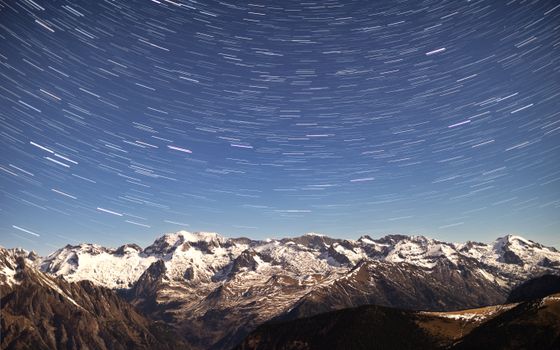 Captivating night sky with star trails swirling above snow-capped mountains. A breathtaking natural panorama.