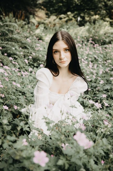 A woman in a flowing white dress sits gracefully amidst a field of wildflowers, exuding serenity.