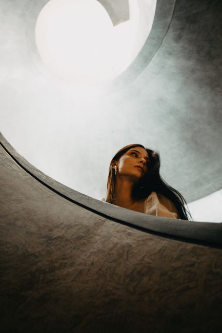 A striking portrait of a woman gazing up through dramatic spiral architecture, infused with light.