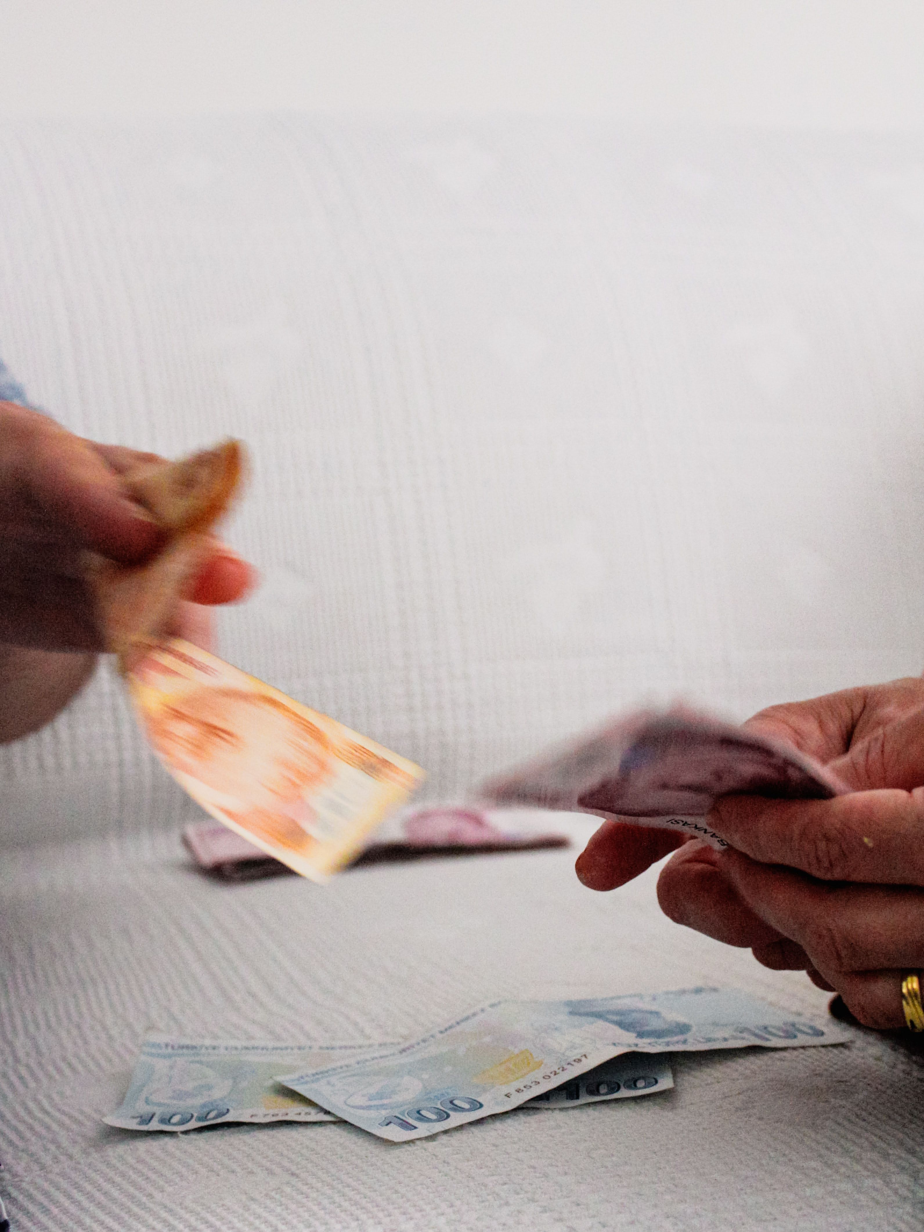 Close-up of hands exchanging currency notes on a white sofa, symbolizing financial transaction.