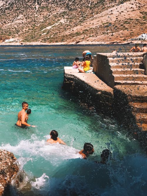 Free A vibrant scene of people enjoying a swim by the rocky Greek coastline on a sunny day. Stock Photo
