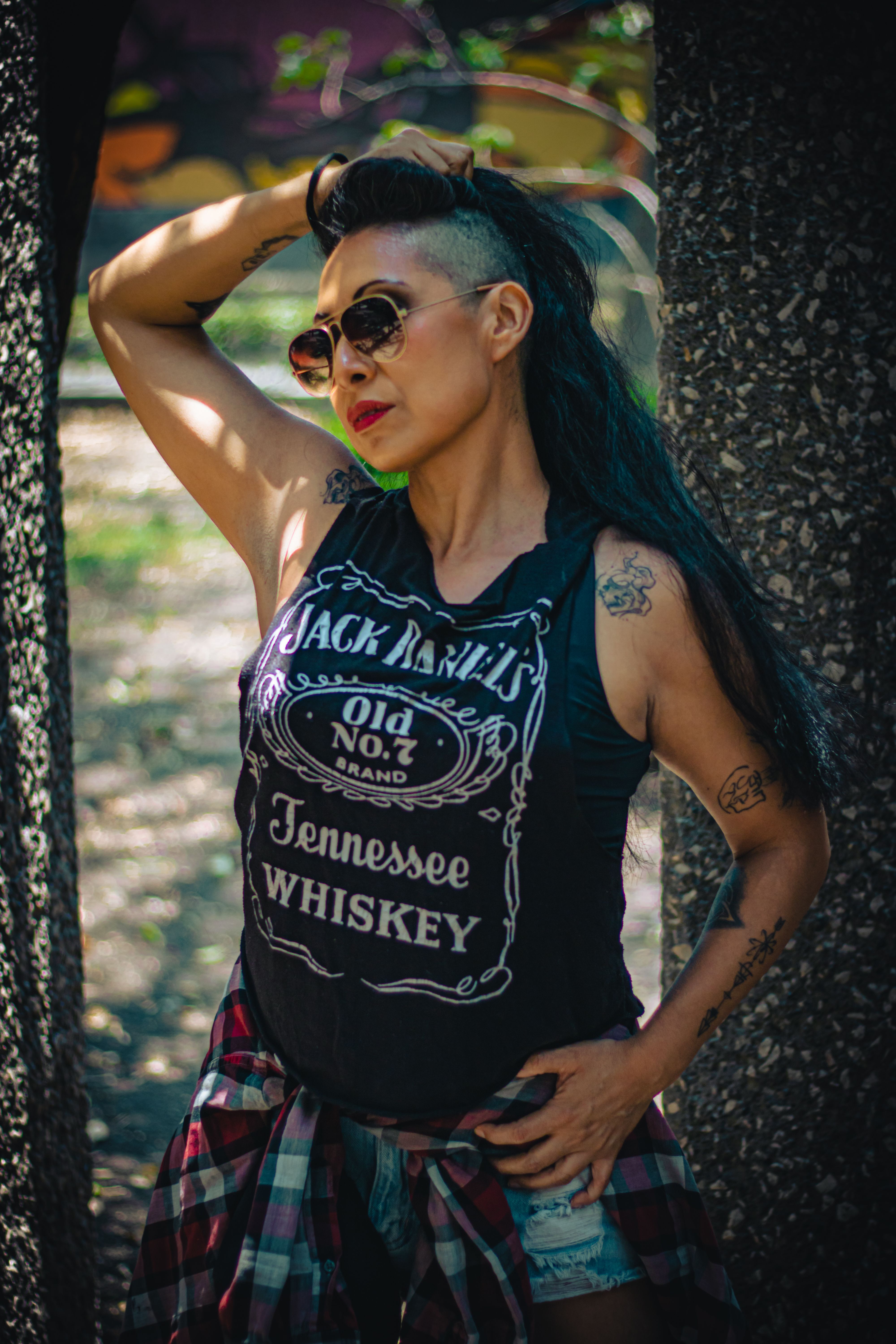 Portrait of a stylish woman in a park wearing sunglasses and tattoos. Urban fashion and confidence.