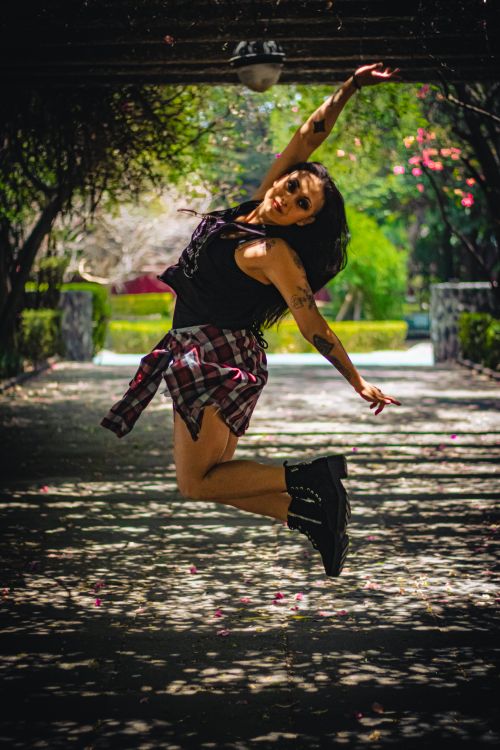 Free Dynamic portrait of a tattooed woman energetically leaping under a grove in Mexico City park. Stock Photo