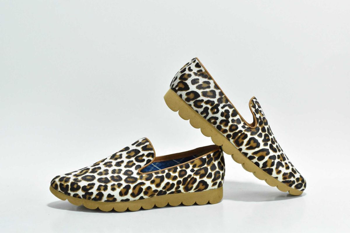 Pair of leopard print slip-on loafers with a cream base and brown rosette spots photographed in a studio setting