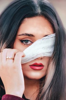 Close-up portrait of a young woman with a bandage over one eye, showcasing glamour and mystery.