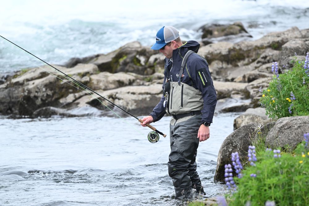fly angler in waders holding a fly rod and reel in a river, the rod blank and grip in sharp focus