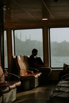 A solitary man sits on a ferry in Istanbul at sunset, reflecting in the warm light.