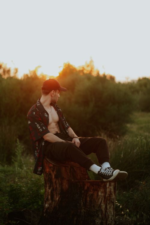 Free A man seated on a tree stump enjoying the sunset in a natural setting, capturing a peaceful moment. Stock Photo