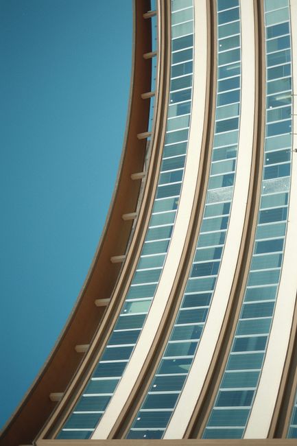 Close-up of a modern curved building with blue glass windows against a clear sky.
