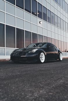 Sleek black Nissan 350Z car parked alongside a glass modern office building.