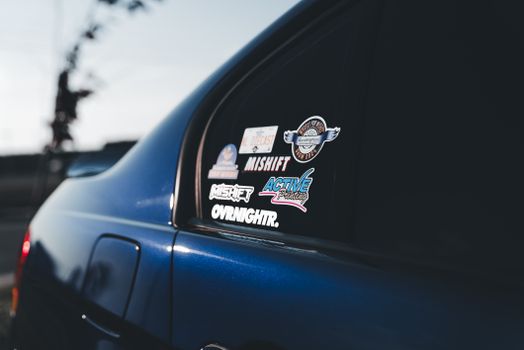 A detailed view of a blue car adorned with racing stickers on the window, captured outdoors.