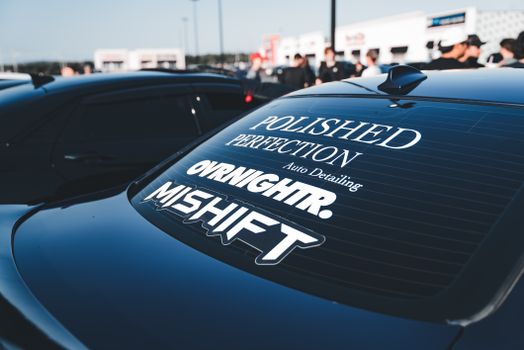 Rear view of black car with custom window decals at an outdoor auto event.