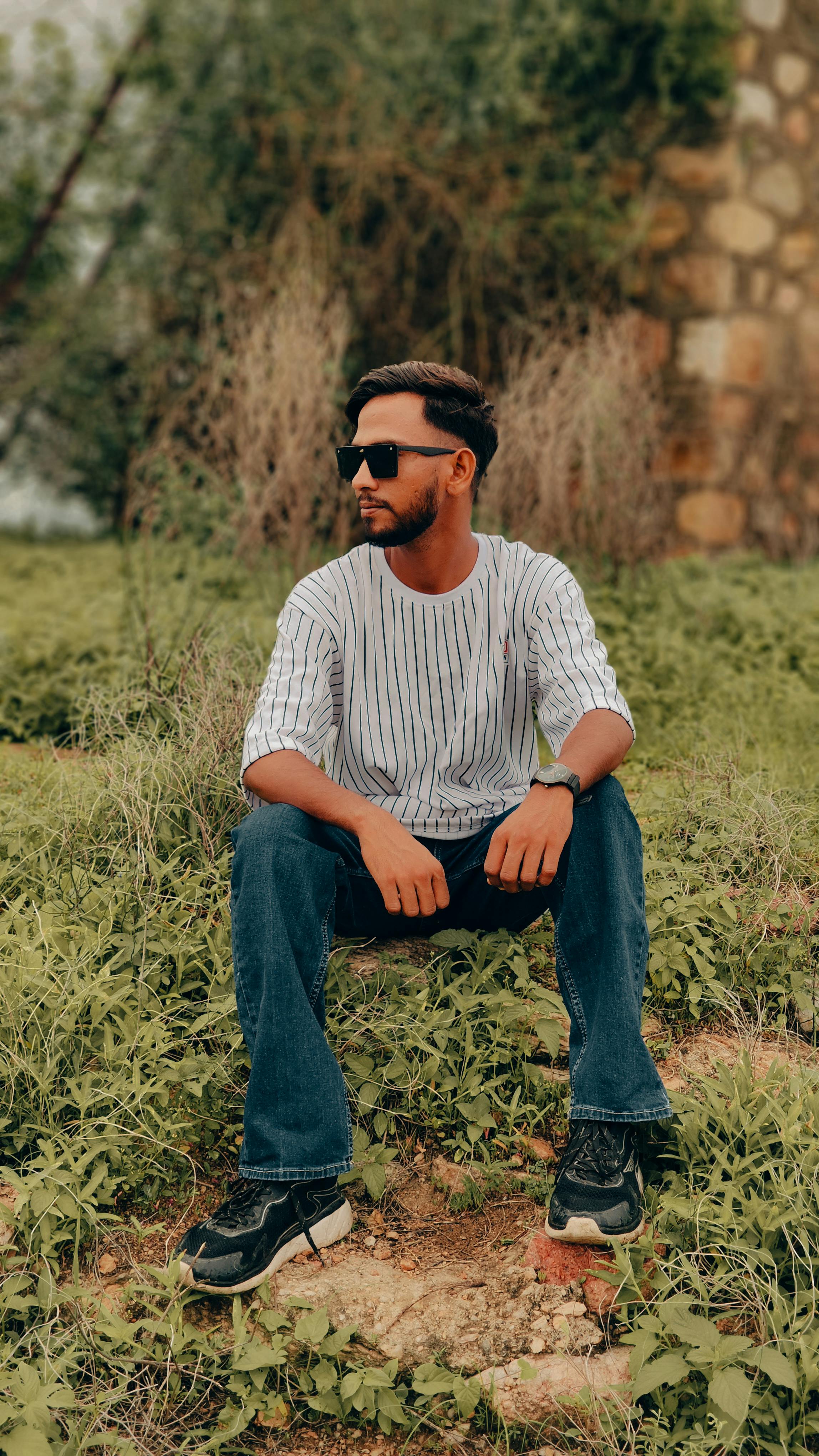 A young man with sunglasses sitting in a lush green park, enjoying leisure time in Jaipur.