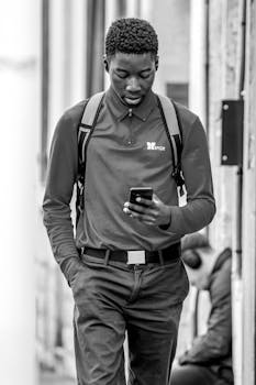 Black and white photo of a young man using a smartphone while walking in the city.