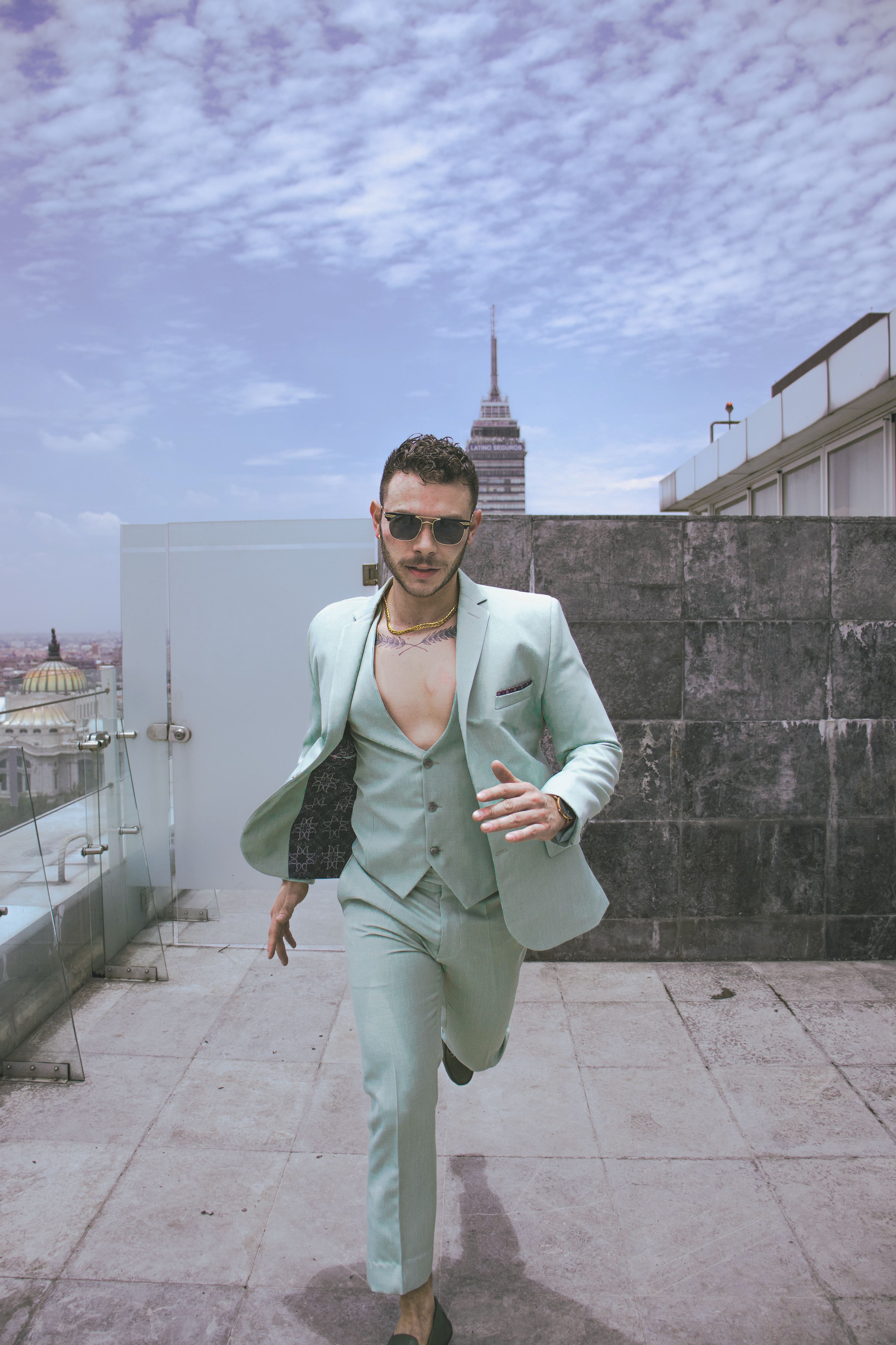 Fashionable man in pastel suit on a rooftop with city skyline. Modern urban style.