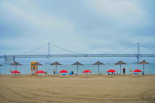 Free Relaxing beach scene featuring Gwangan Bridge in Korea with umbrellas and a lifeguard stand. Stock Photo