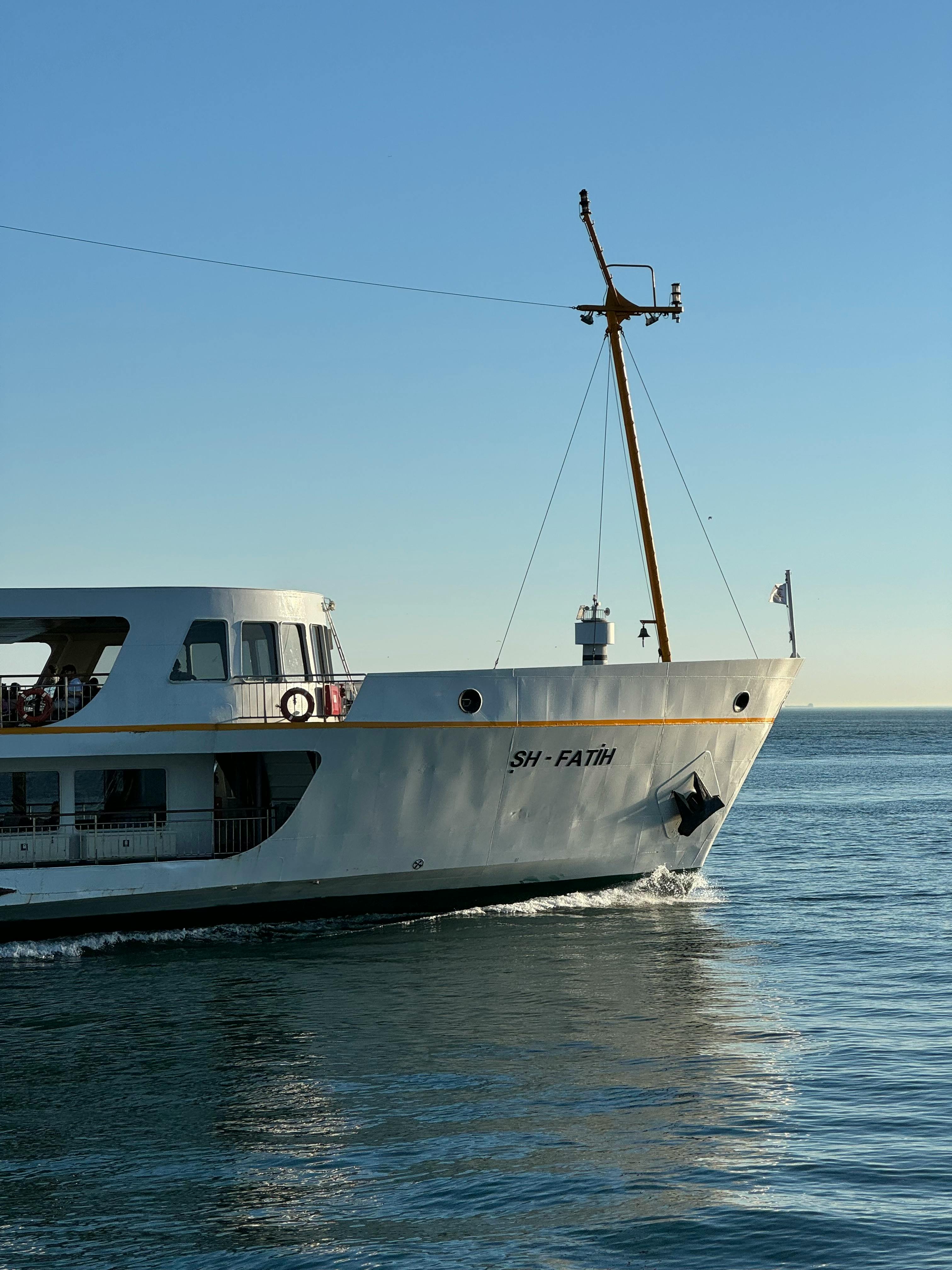 A white passenger vessel identified as SH-Fatih gracefully sails across a calm sea under a clear sky.