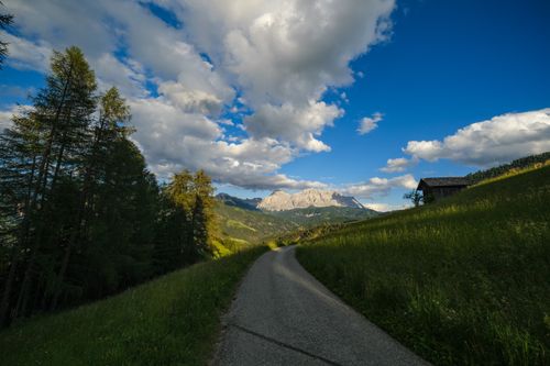 Free A picturesque road through a lush mountainous landscape under a vibrant blue sky. Stock Photo