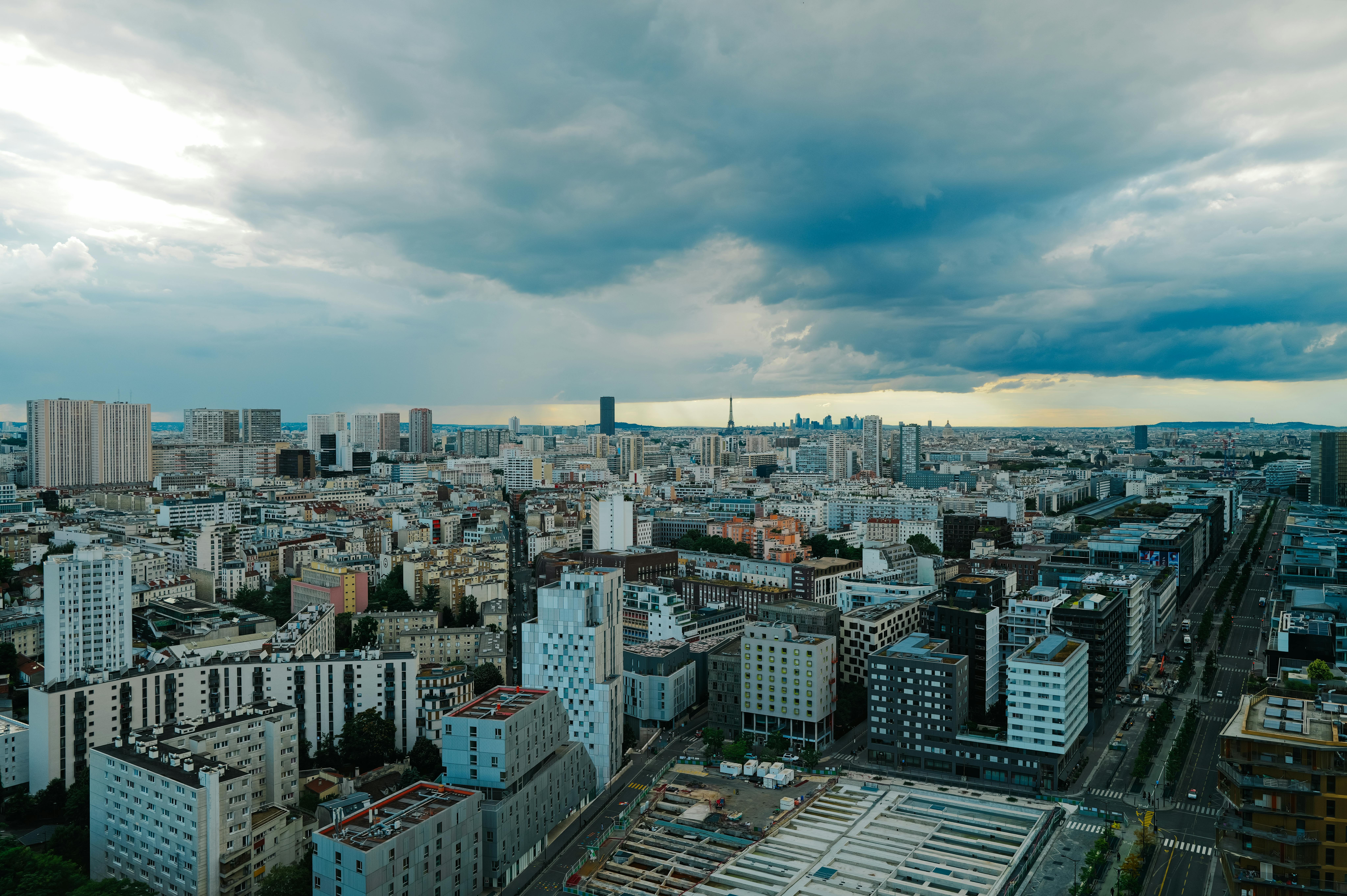 Panoramic aerial view of a modern city skyline under dramatic clouds at twilight.