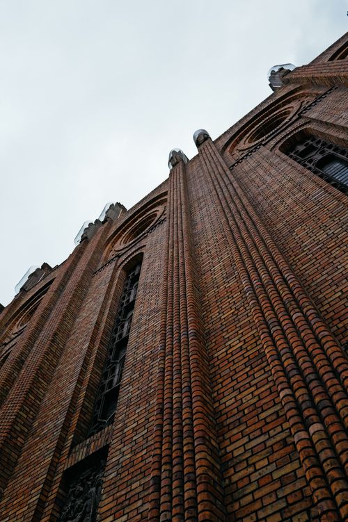 Free Low angle view of a Gothic-style brick cathedral tower under cloudy skies. Stock Photo