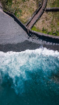 Stunning aerial shot of turquoise waves crashing on the rocky shore at San Jorge, Madeira, Portugal.