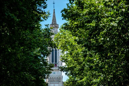 Gothic tower spire surrounded by lush green trees in a Nantes park, France.