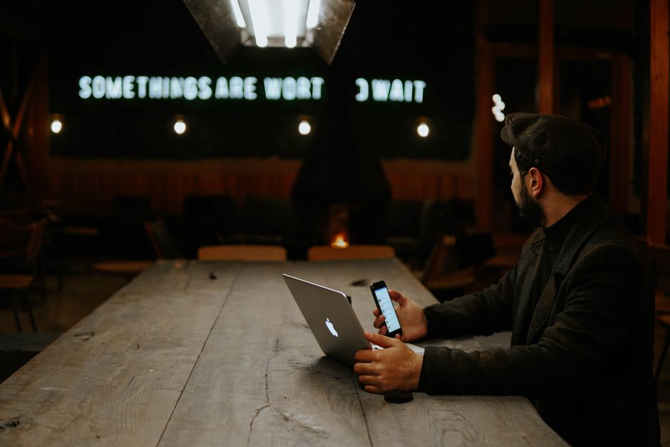Man using laptop and smartphone in a cozy cafe setting at night, showcasing modern remote work.