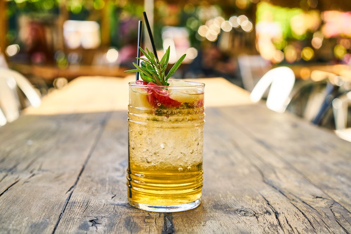 Free Sparkling beverage with rosemary garnish in a glass on a wooden table outdoors. Stock Photo