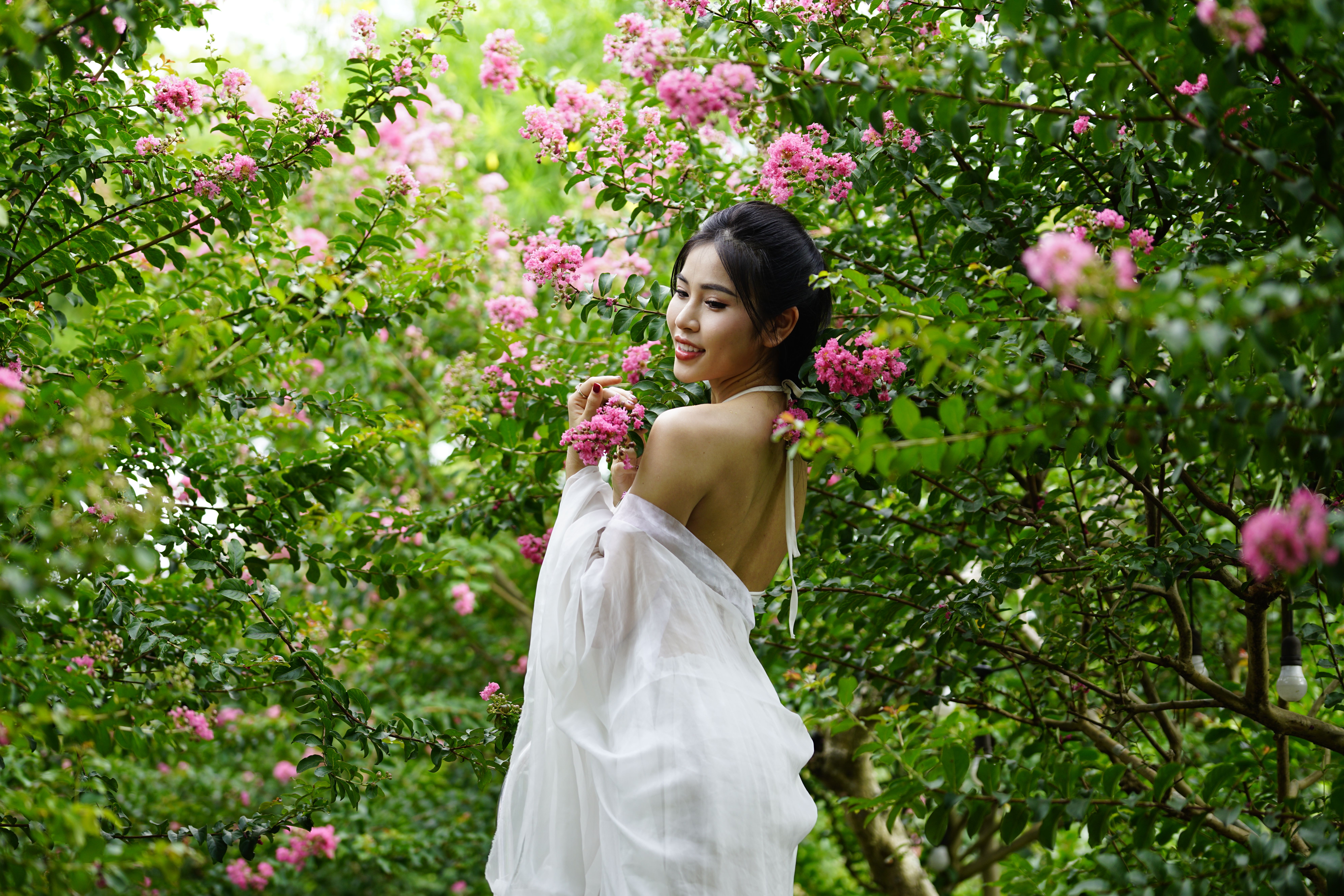 A woman in a white dress is standing in a garden with pink flowers ...