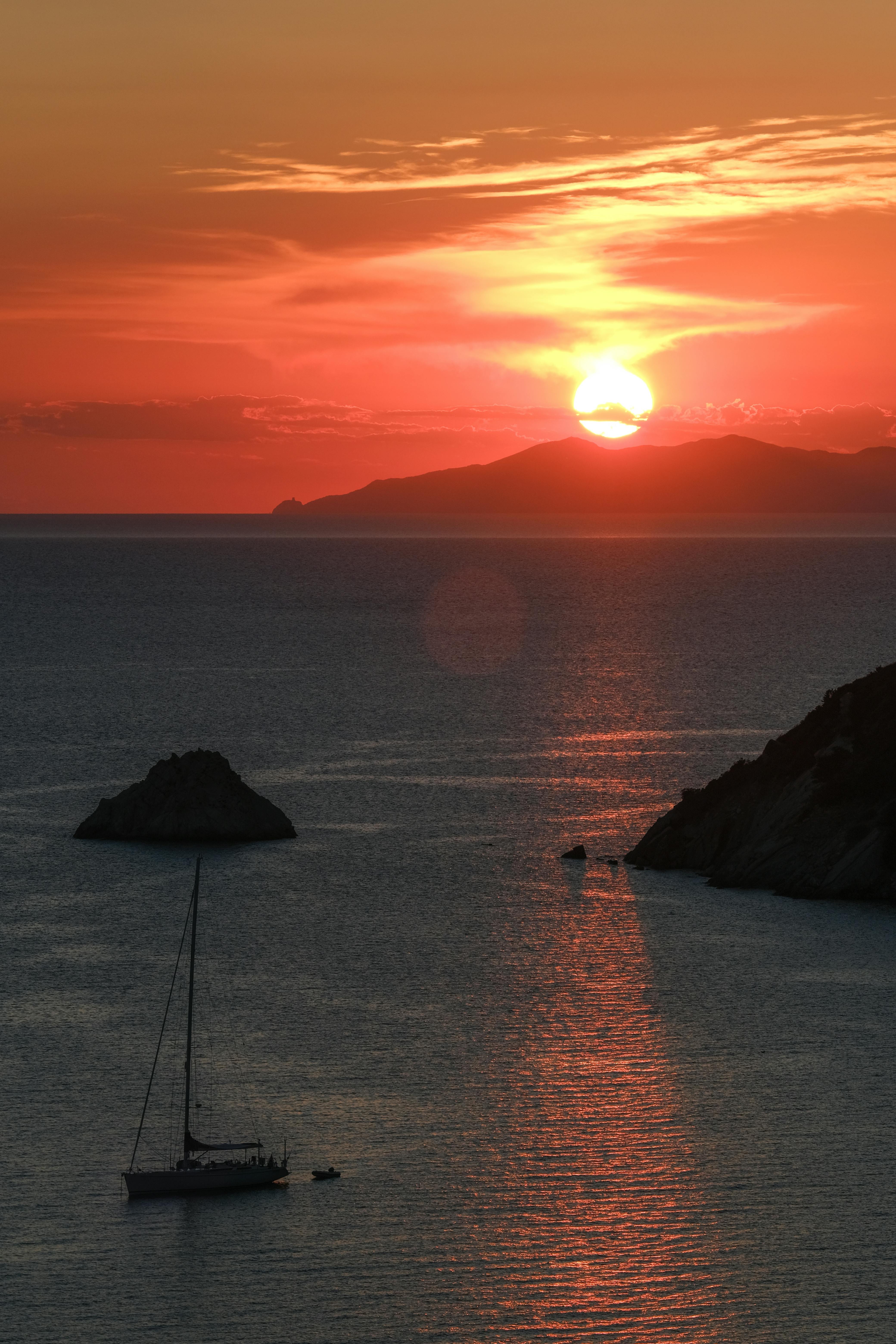 A tranquil sunset scene with a sailboat on the ocean, reflecting warm hues.