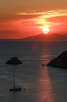 A tranquil sunset scene with a sailboat on the ocean, reflecting warm hues.
