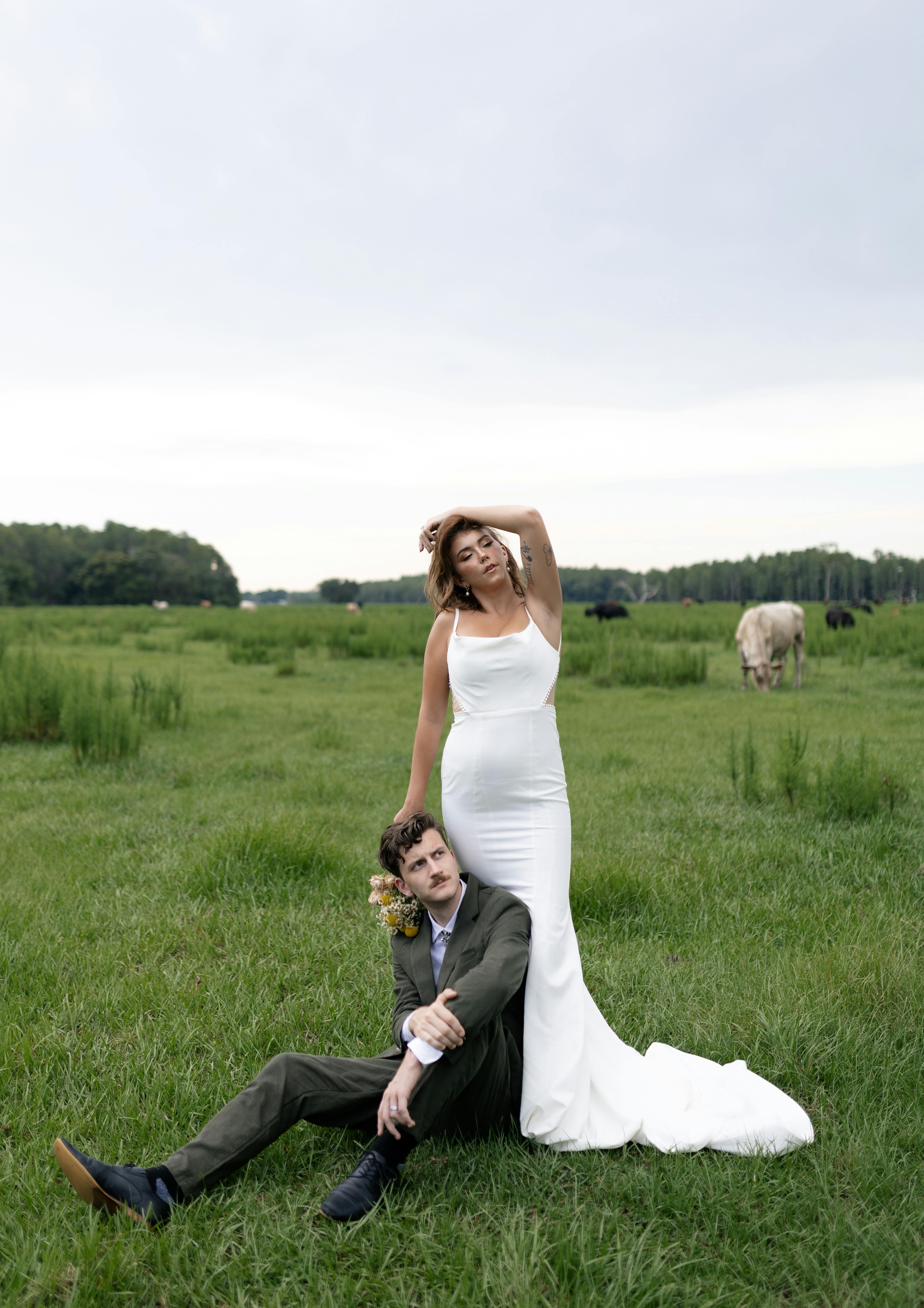 a bride and groom pose in a field with cows