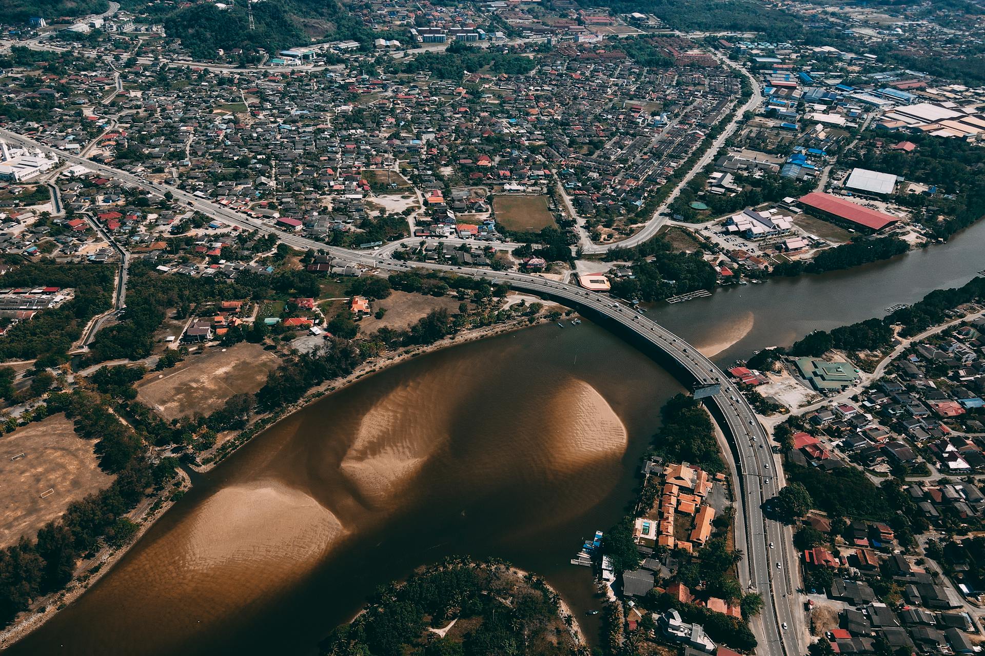 Stunning aerial view of a cityscape featuring a winding river and a modern bridge crossing through urban development.