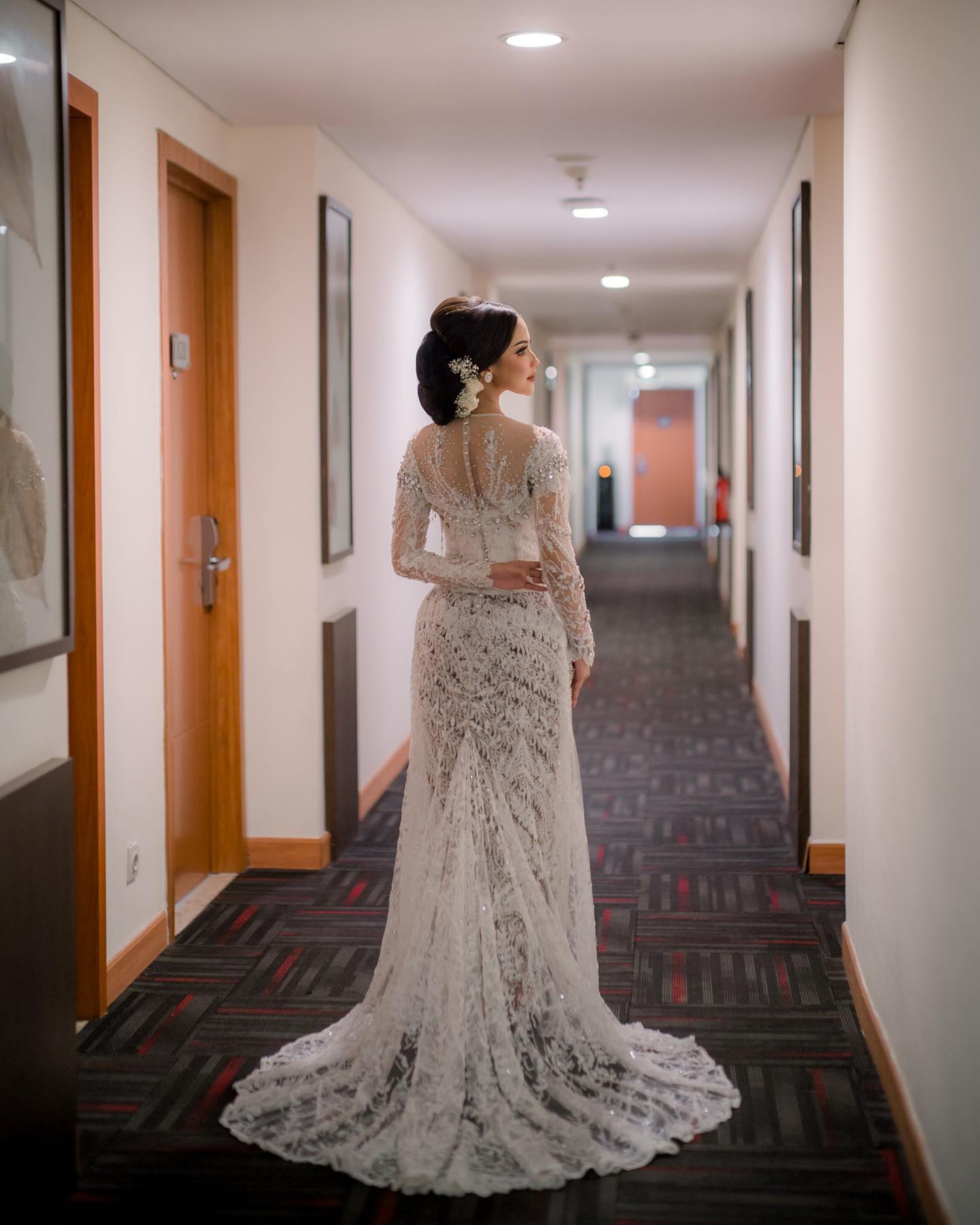 Bride in a luxurious lace gown stands in a corridor, showcasing elegance and glamour before her wedding ceremony.