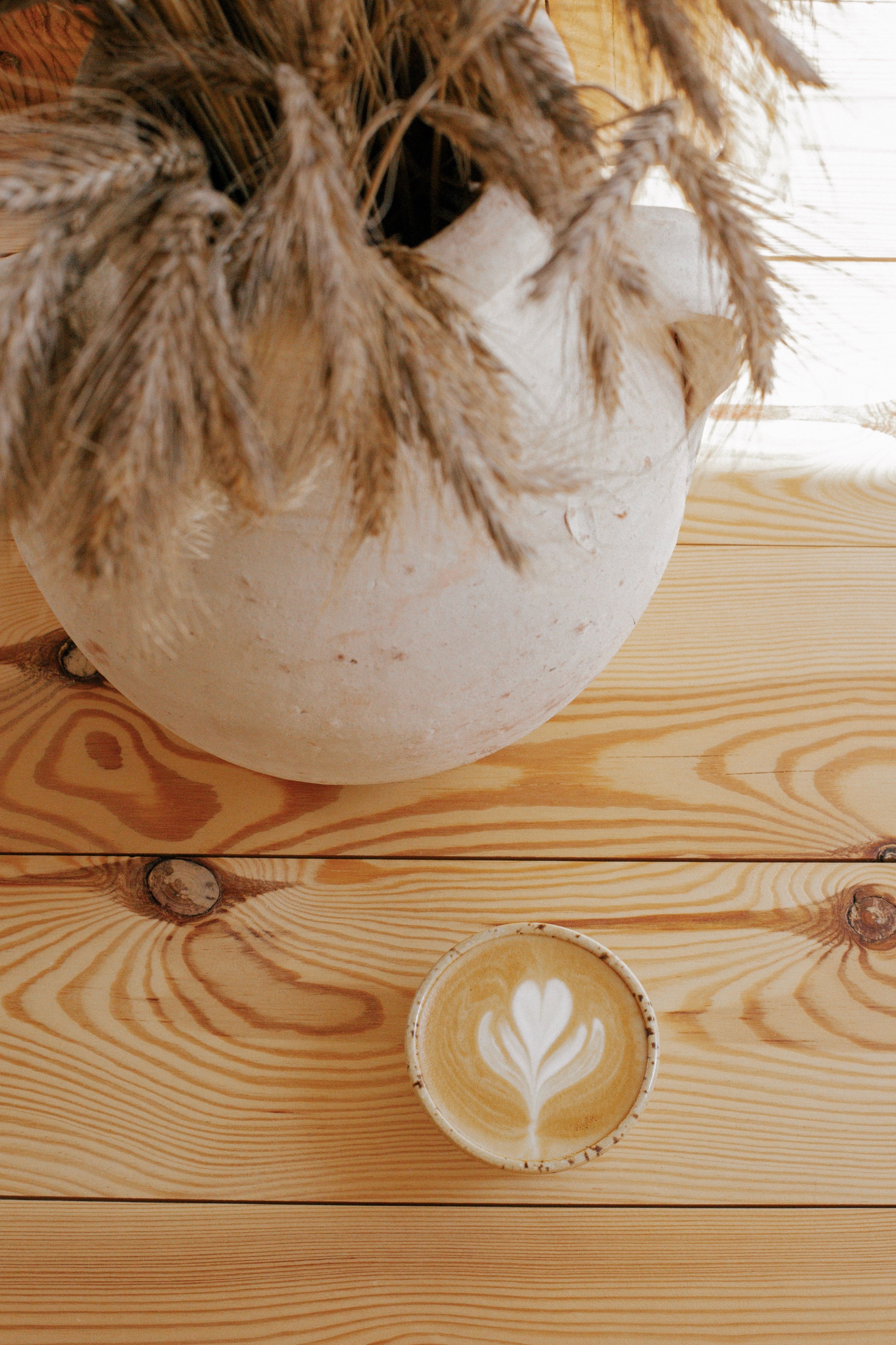 Top view of a beautiful latte art coffee surrounded by rustic wheat decor on a wooden table.